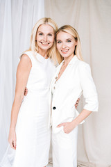 smiling elegant blonde mother and daughter in total white outfits