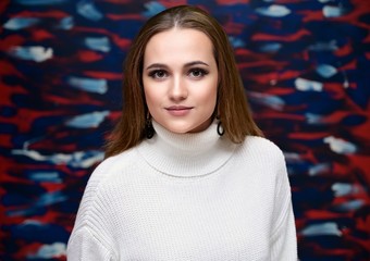 A close-up portrait of a pretty brunette girl with beautiful hair, excellent make-up, beautiful face skin in a white jacket on a colored background. Made in the studio.