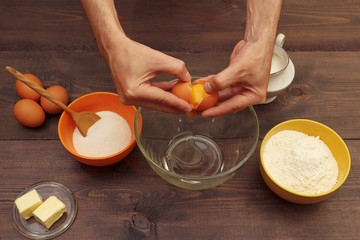 Baker hands break an egg over a bowl on a wooden table.