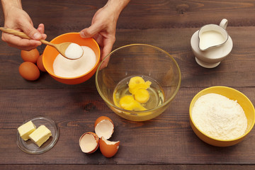 Baker hands pour sugar into a bowl for making dough on a wooden table.
