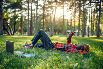 Black student with phone lying on the grass