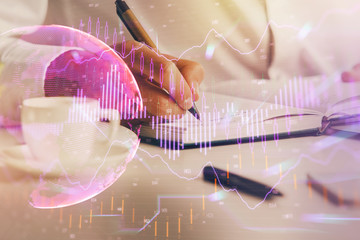 Double exposure of man's hands writing notes of stock market with forex chart.