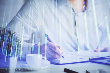 Double exposure of man's hands writing notes of stock market with forex chart.