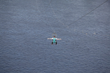 Rear view of young man riding on zip line against a background of a blue river water wave, Kyiv, Ukrainee