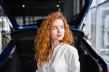 Fototapeta na wymiar Portrait of a beautiful red-haired girl on the background of the car
