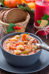 Soup with turkey, pasta, carrot, celery, tomato and cannellini beans, garnished with parmesan cheese, on the table with autumn decoration, US Thanksgiving harvest feast, vertical, closeup