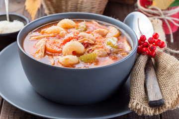 Soup with turkey, pasta, carrot, celery, tomato and cannellini beans, garnished with parmesan cheese, on the table with autumn decoration, US Thanksgiving harvest feast, horizontal, closeup