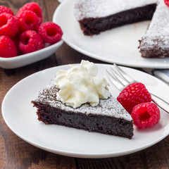 Chocolate sticky brownie cake, swedish dessert Kladdkaka, on the plate, garnished with icing sugar and raspberry,  square format