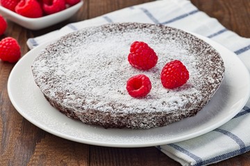 Chocolate sticky brownie cake, swedish dessert Kladdkaka, on the plate, garnished with icing sugar and raspberry,  horizontal