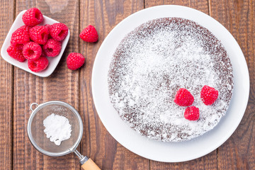 Chocolate sticky brownie cake, swedish dessert Kladdkaka, on the plate, garnished with icing sugar and raspberry, horizontal, top view