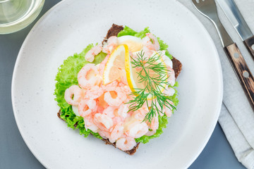 Traditional savory swedish sandwich with a dark bread, lettuce, eggs, mayonnaise, shrimps, dill and lemon, horizontal, top view