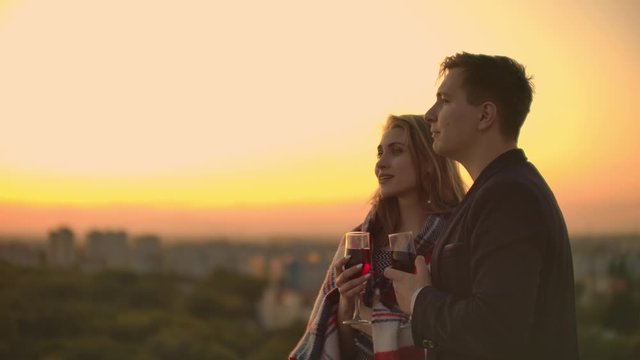 Lovers embracing guy girl watching the sunset with wine standing on the roof of the building. Slow motion picture of the relationship of a married young couple