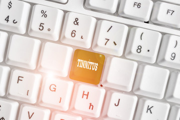Word writing text Tinnitus. Business photo showcasing A ringing or music and similar sensation of sound in ears White pc keyboard with empty note paper above white background key copy space