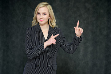 Portrait of a pretty young blonde girl with beautiful hair, excellent make-up, perfect face skin in a business suit on a dark background. Made in the studio.