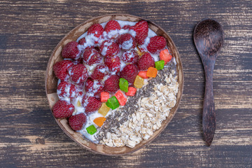 Smoothie in coconut bowl with raspberries, oatmeal, candied fruit and chia seeds for breakfast , close up. The concept of healthy eating, superfood