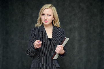 Portrait of a pretty young blonde girl with beautiful hair, excellent make-up, perfect face skin in a business suit on a dark background. Made in the studio.