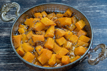 Baked yellow pumpkin with honey, anise, olive oil and spices on a plate on the wooden table. Vegetarian food. Closeup