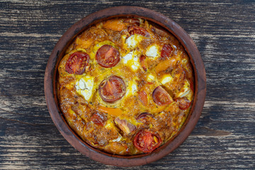 Ceramic bowl with vegetable frittata, simple vegetarian food. Frittata with tomato, pepper, onion and feta cheese on wooden table, close up. Italian egg omelette