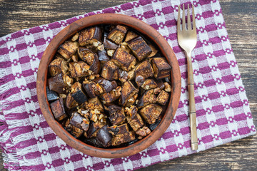 Baked eggplant with walnut, olive oil and spices on a plate on the wooden table. Vegetarian food. Close up