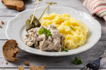 Beef Stroganoff, traditional Russian dish of goulash with beef in creamy sauce, mashed potatoes and pickles. Serve with rustic bread