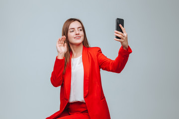 Naklejka premium girl in a red jacket takes a selfie on the phone on a gray background