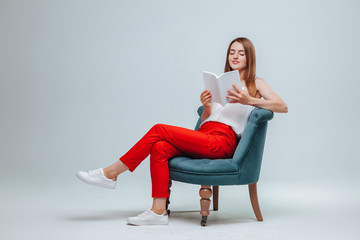 Girl in red pants sitting in a chair and reading a book with a white cover