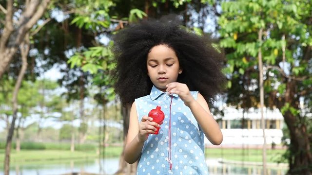 afro little kid cute girl blowing soap bubbles in summer park outdoors . Multi-ethnic children . Different ethnicity kid . african american , mixed race  , leisure playful
