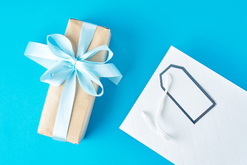 White shopping bag with gift box on blue background, top view