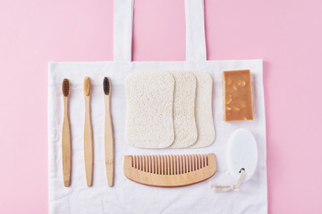 Body care natural wooden eco friendly products on a pink background, flat lay top view. Bamboo toothbrushes, wooden comb, soap, spongle and natural washclothers. Zero waste concept