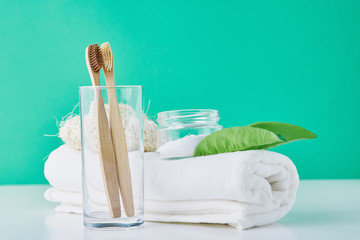 Wooden bamboo toothbrushes in glass, baking soda and towel on a green background. Personal hygiene concept