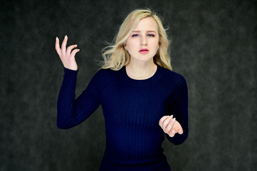 Portrait of a pretty young slim blonde girl with beautiful fluttering hair, great makeup, in a dark blue dress on a dark background. Made in the studio.