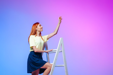 Red-haired girl stands at the top of the stairs and stretches her hand on a pink and blue background