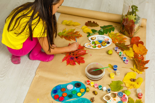Girl paints leaves. Gouache, brush and various autumn leaves, Children's art project. Colorful Hand-painted on dry autumn leaves
