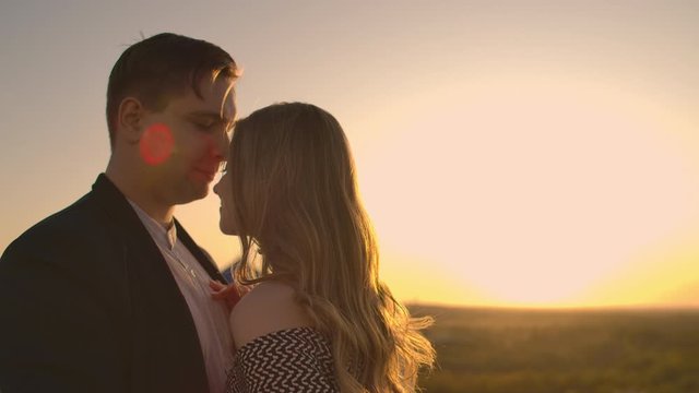 A man and a woman embrace on a rooftop at sunset