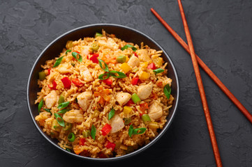 Schezwan Chicken Fried Rice in black bowl at dark slate background. Szechuan Rice is indo-chinese cuisine dish with bell peppers, green beans, carrot, chicken breasts.