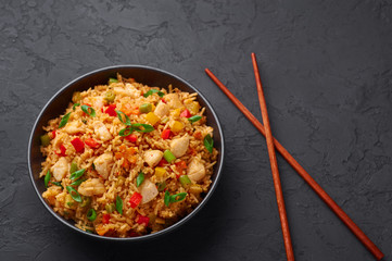 Schezwan Chicken Fried Rice in black bowl at dark slate background. Szechuan Rice is indo-chinese cuisine dish with bell peppers, green beans, carrot, chicken breasts. Copy space