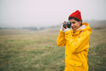 Young woman in yellow raincoat photographing foggy scenery