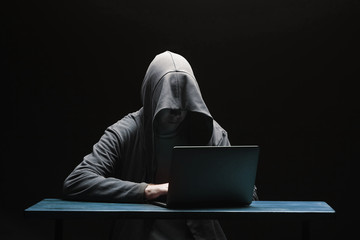 Hacker in a hood with a laptop on a black background