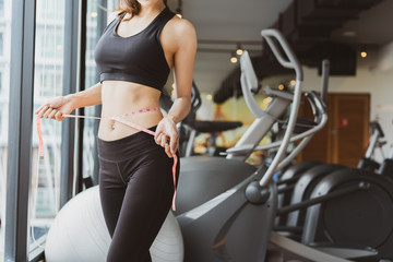 Closeup woman slim athlete using body fat measurement and waist size with waist line after workout...