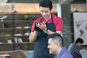 asian male waiter write orders from costumers at cafe in background