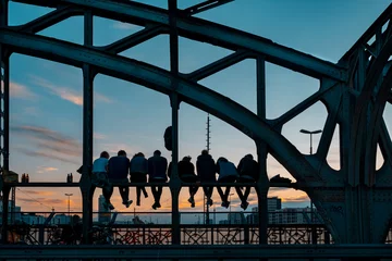 Hintergrundbeleuchtung mehrerer Personen, die auf der Hackerbrücke in München sitzen und auf den Sonnenuntergang warten © ikuday