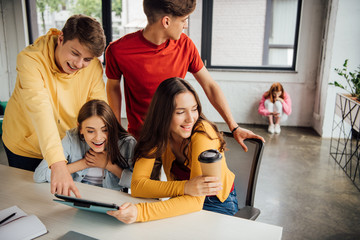 group of smiling schoolchildren using digital tablet in classroom