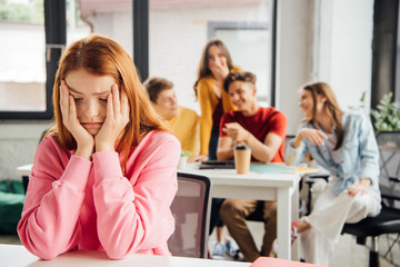 sad girl sitting in front of laughing classmates