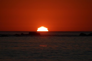 Naklejka na ściany i meble sun reaching the horizon in the sea on a red sky sunset