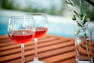 two glasses of rose wine with  olives against blue water on a pier..