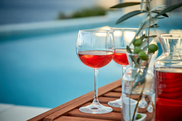 two glasses of rose wine with  olives against blue water on a pier..