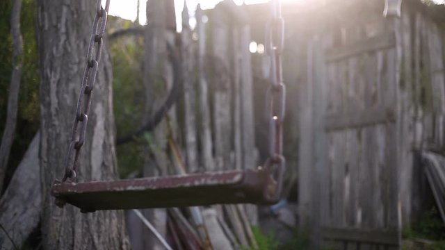 Wooden swing with metal chains rocking in  the village yard. Sunny summer background. Parental home concept