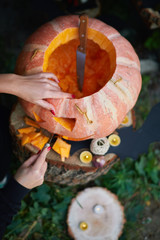 Young fair-skinned girl with red nails carving a face on a pumpkin. Creating traditional decoration for Halloween and Thanksgiving Day