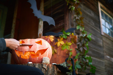 Young fair-skinned girl with red nails carving a face on a pumpkin. Creating traditional decoration for Halloween and Thanksgiving Day