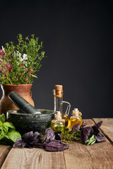 grey mortar near clay vase with herbs on wooden table isolated on black